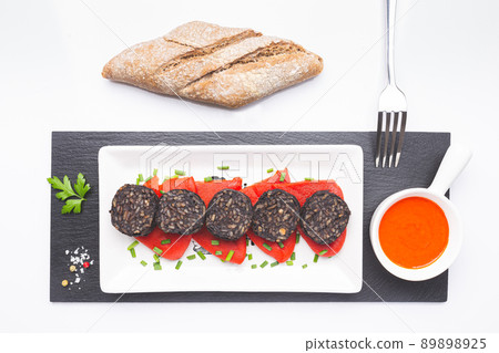 Slices of Spanish black pudding on piquillo peppers in white plate on white background. Spanish tapas. 89898925