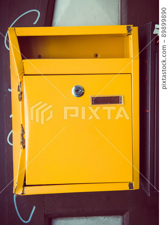 Yellow mailbox on the wall at sunny day. Box for letters and correspondence, vertical orientation 89899890