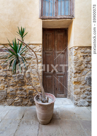 Abandoned stone bricks wall with wooden door, wrought iron window and planting pot 89900078