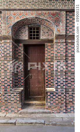 Wooden grunge decorated arched gate with inner small door on wall with black and red bricks 89900131