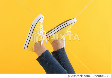 Female legs in jeans and sneakers on yellow background 89900627