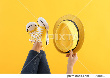 Female legs in jeans and sneakers, and female hand holding hat on yellow background 89900628
