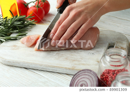 Female hands cut raw chicken fillet on wooden board 89901309