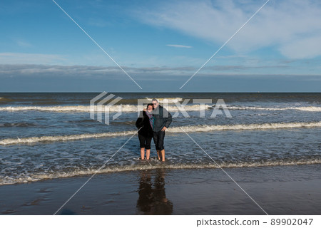 Man and woman in their thirties standing with their feet in the sea Man and woman in their thirties standing with their feet in the sea 89902047