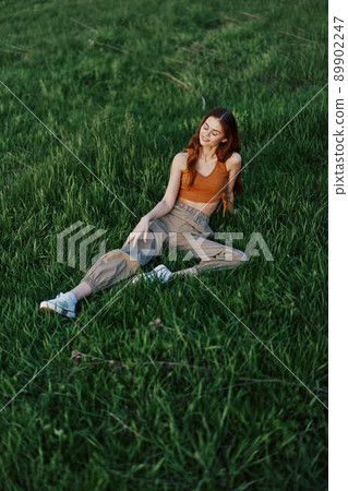 A woman lies on fresh spring green grass in a park without mosquitoes or ticks and enjoys relaxing while watching the sunset. The concept of safe outdoor recreation 89902247