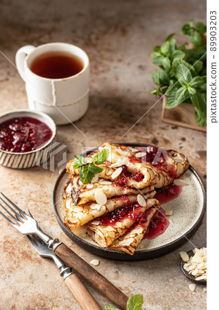 Crepes with raspberry jam, almond petals and a mint leaf in brown plate. Breakfast composition Crepes with raspberry jam, almond petals and a mint leaf in brown plate. Breakfast composition 89903203