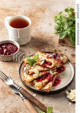 Crepes with raspberry jam, almond petals and a mint leaf in brown plate. Breakfast composition Crepes with raspberry jam, almond petals and a mint leaf in brown plate. Breakfast composition 89903205