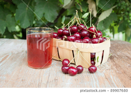 Cherry berry. Harvest cherries in a basket on a wooden background. A glass of fresh cherry juice, fruit drink. Cherry berry. Harvest cherries in a basket on a wooden background. A glass of fresh cherry juice, fruit drink. 89907680