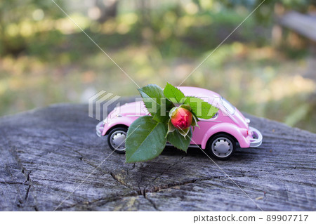 Toy pink car on wooden background with red rose branch 89907717