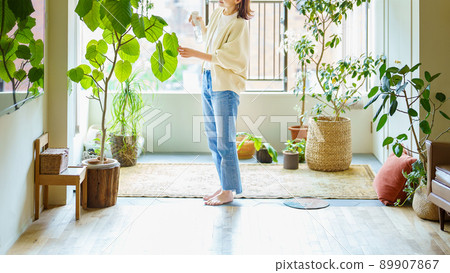 A woman watering a houseplant in a room 89907867