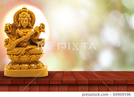Saraswati statue carved in brown wood on a wooden table has a natural bokeh background with a powerful light behind the head 89909596