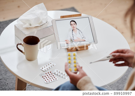 High angle shot of unrecognizable woman having online appointment with doctor using digital tablet holding pills and thermometer 89910997