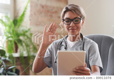 Young adult female doctor wearing eyeglasses sitting at desk starting online consultation greeting patient on video call Young adult female doctor wearing eyeglasses sitting at desk starting online consultation greeting patient on video call 89911078