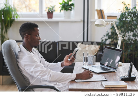 Medium side view portrait of modern young adult Black doctor wearing white coat and eyeglasses Medium side view portrait of modern young adult Black doctor wearing white coat and eyeglasses 89911129
