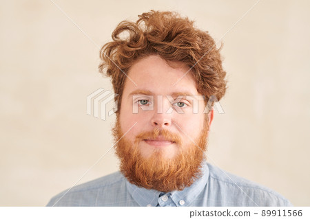Portrait of serious redhead young student guy with beard and mustache having curly hair standing against beige background 89911566