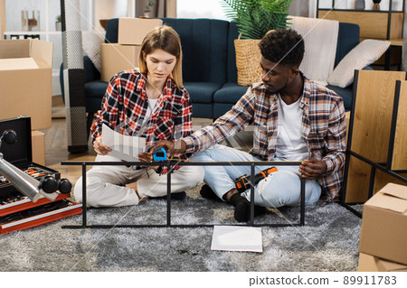 Beautiful multi ethnic couple using tools for arranging home Beautiful multi ethnic couple using tools for arranging home 89911783