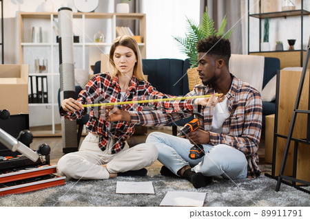 Diverse couple using measuring tape at new apartment Diverse couple using measuring tape at new apartment 89911791