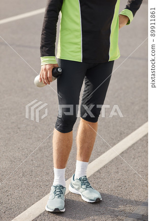 Lower body shot of unrecognizable fit man wearing tracksuit standing on track with bottle of water 89911861
