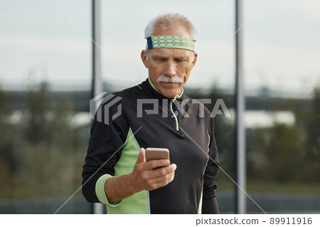 Horizontal waist up portrait of modern senior man wearing tracksuit using his smartphone Horizontal waist up portrait of modern senior man wearing tracksuit using his smartphone 89911916