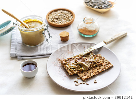 Homemade sunflower seed spread in jar with roasted seeds, maple syrup, cinnamon, crisp bread on light background 89912141