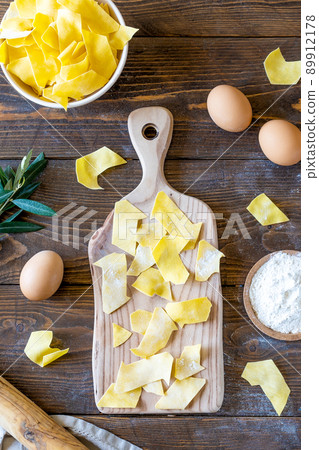 Homemade raw pasta Maltagliati on cutting board with ingredients on wooden background. Top view Homemade raw pasta Maltagliati on cutting board with ingredients on wooden background. Top view 89912178