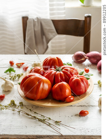 Red tomatoes on the plate and white wooden background with oregano, basil leaves, garlic and onion.  89912205