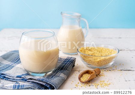 Millet milk in glass, glass jar and bowl on white wooden table with blue background Millet milk in glass, glass jar and bowl on white wooden table with blue background 89912276