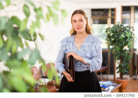 Portrait of woman holding briefcase in her hands in office 89915760
