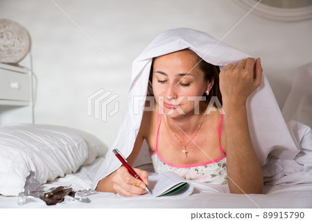 Woman elaxing under blanket and making schedule for tomorrow 89915790