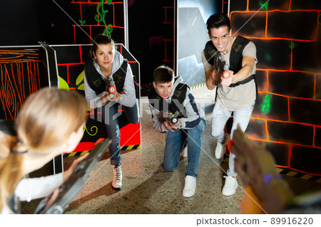 Excited young people playing enthusiastically laser tag game two teams opposite each other in dark room 89916220