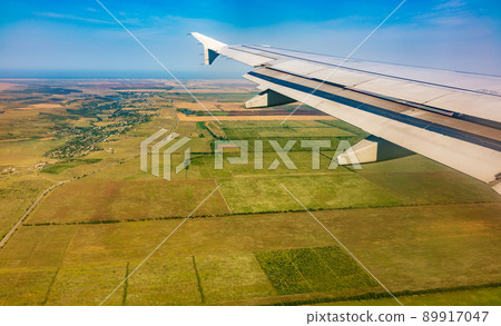 View of airplane wing, blue skies and green land during landing. Airplane window view. 89917047
