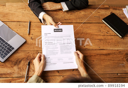 Top view of businesswoman holding resume and giving to female candidate during corporate meeting or job interview. Top view of businesswoman holding resume and giving to female candidate during corporate meeting or job interview. 89918194