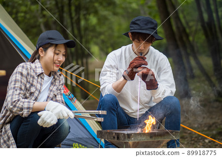 一個用噴火棒點燃篝火的男孩和一個幫忙的女朋友 89918775