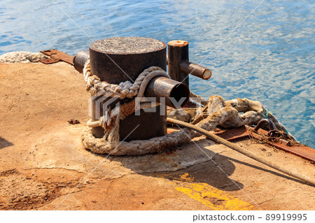 Mooring bollard entwined with a mooring rope by the pier at seaside Mooring bollard entwined with a mooring rope by the pier at seaside 89919995
