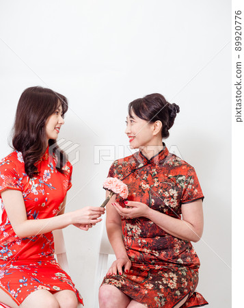 Portrait of asian young daughter and mother wearing traditional cheongsam qipao and smiling with flowers carnation in hands isolated on white background. 89920776