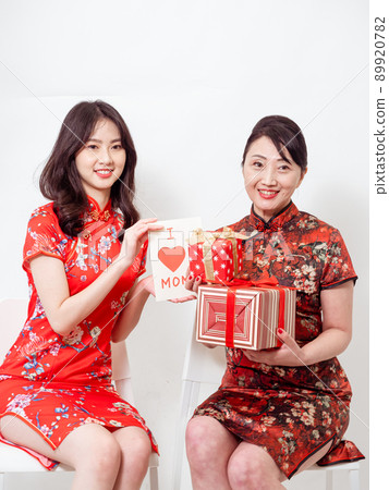 Daughter wearing traditional cheongsam qipao is congratulating mom and giving her Giving Handmade Greeting Card.Family holiday and togetherness. 89920782