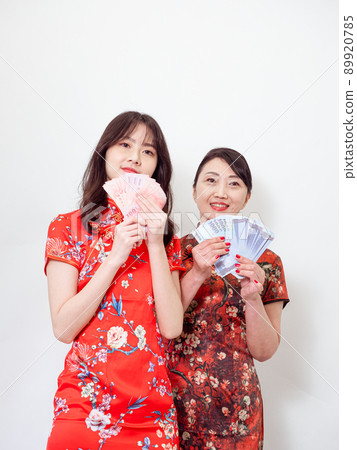 Portrait of mature asian mother and her asian daughter both wearing traditional cheongsam qipao dress holding bunch of money banknotes on white background. Portrait of mature asian mother and her asian daughter both wearing traditional cheongsam qipao dress holding bunch of money banknotes on white background. 89920785