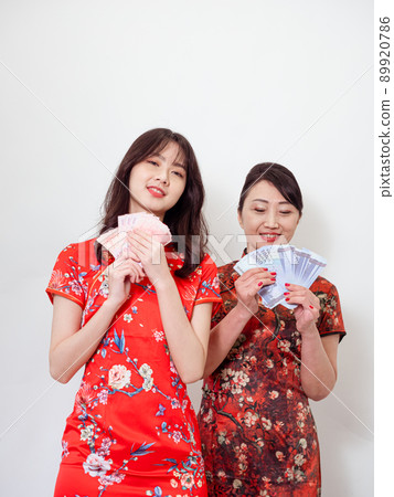 Portrait of mature asian mother and her asian daughter both wearing traditional cheongsam qipao dress holding bunch of money banknotes on white background. Portrait of mature asian mother and her asian daughter both wearing traditional cheongsam qipao dress holding bunch of money banknotes on white background. 89920786