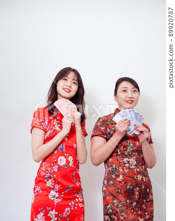 Portrait of mature asian mother and her asian daughter both wearing traditional cheongsam qipao dress holding bunch of money banknotes on white background. Portrait of mature asian mother and her asian daughter both wearing traditional cheongsam qipao dress holding bunch of money banknotes on white background. 89920787