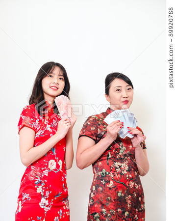 Portrait of mature asian mother and her asian daughter both wearing traditional cheongsam qipao dress holding bunch of money banknotes on white background. Portrait of mature asian mother and her asian daughter both wearing traditional cheongsam qipao dress holding bunch of money banknotes on white background. 89920788