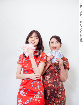 Portrait of mature asian mother and her asian daughter both wearing traditional cheongsam qipao dress holding bunch of money banknotes on white background. 89920789