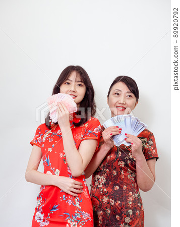 Portrait of mature asian mother and her asian daughter both wearing traditional cheongsam qipao dress holding bunch of money banknotes on white background. Portrait of mature asian mother and her asian daughter both wearing traditional cheongsam qipao dress holding bunch of money banknotes on white background. 89920792