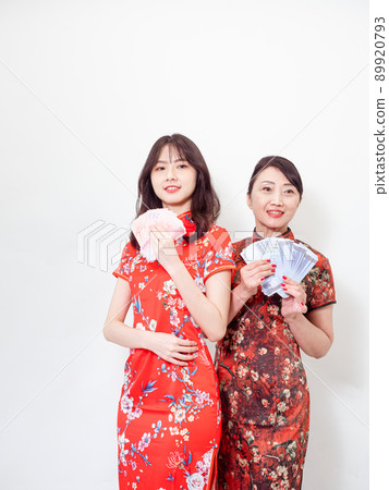 Portrait of mature asian mother and her asian daughter both wearing traditional cheongsam qipao dress holding bunch of money banknotes on white background. Portrait of mature asian mother and her asian daughter both wearing traditional cheongsam qipao dress holding bunch of money banknotes on white background. 89920793