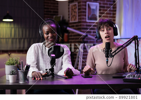 POV of happy women talking to audience on podcast show, filming live discussion on camera to create channel content. Female influencers meeting in studio to record video episode. 89921801