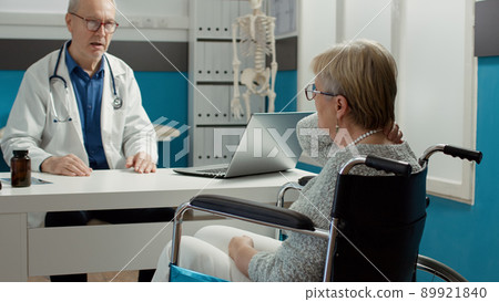 General practitioner consulting woman with chronic disability in medical office, doing checkup examination with medication. Retired patient with impairment and health condition at appointment. General practitioner consulting woman with chronic disability in medical office, doing checkup examination with medication. Retired patient with impairment and health condition at appointment. 89921840