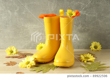 Rubber boots with flowers on wooden table with leaves 89922506