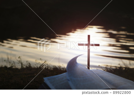 The holy bible and the cross of Jesus Christ on the waterside at sunset symbolize the love of death and resurrection 89922800