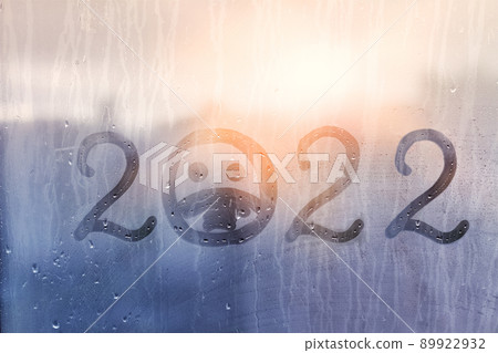hahdmade painted numbers 2022 with sad face in protective medical mask on splashed by rain foggy glass on blue window, concept photo self-isolation, coronavirus, covid - 19 89922932