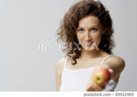 Smiling lovely cute curly beautiful woman in basic white t-shirt pulls apple enjoy healthy food posing isolated on over white background. Natural Eco-friendly products concept. Copy space 89922969