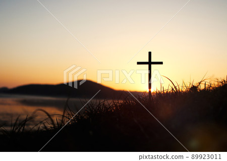 The holy cross of Jesus Christ on the grass with the strong light of the sunset sky symbolizes death and resurrection love 89923011